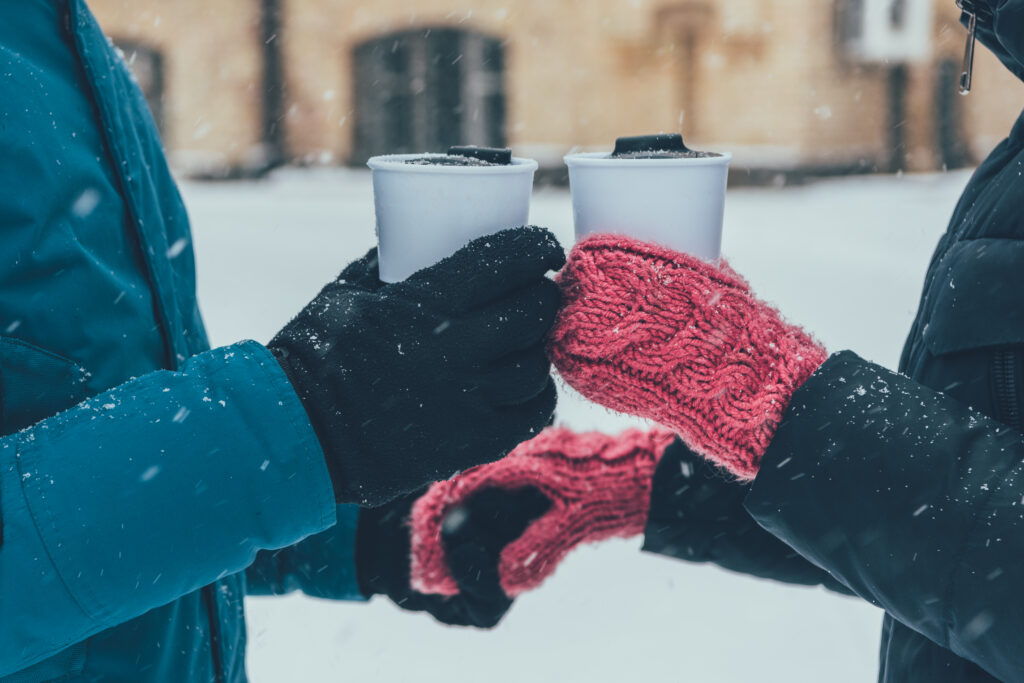 partial view of couple with hot drinks holding hands on street in winter