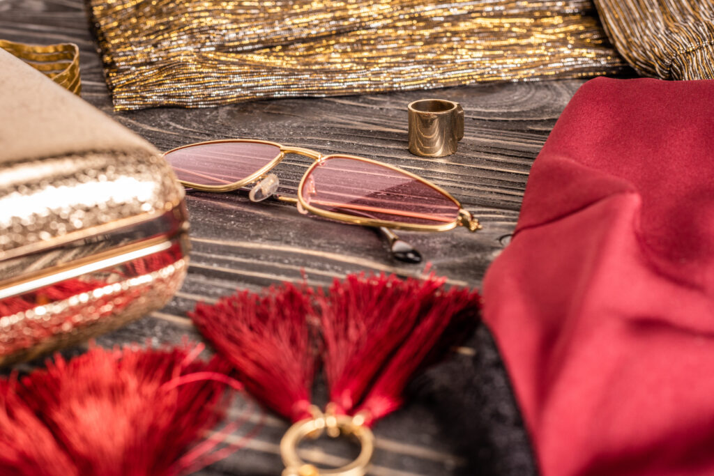 close up view of fashionable feminine earrings, sunglasses and purse arranged on wooden tabletop