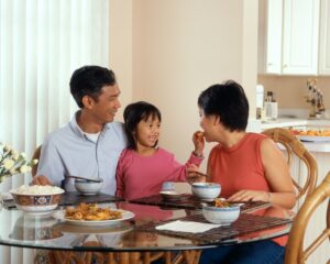 A little girl feeding her mum food whilst on her dad's lap