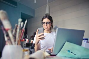 A woman looking at her phone with a laptop in front of her