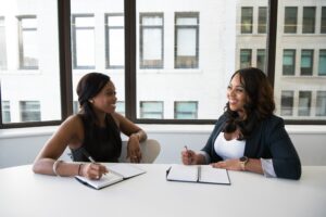 Two women having a conversation with notepads on their desk