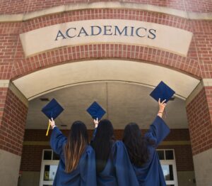 Three girls holding up their graduation hats above their head