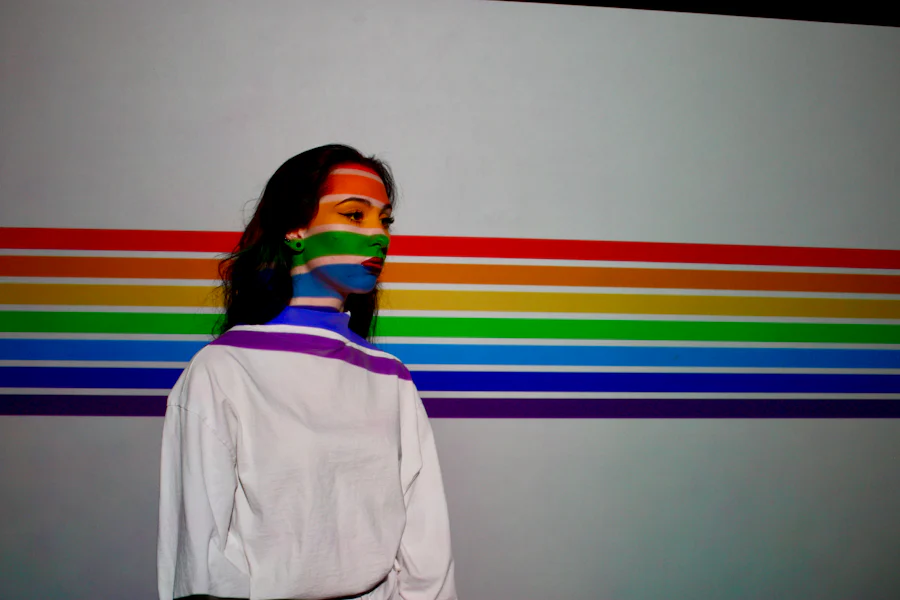 A woman with the LGBTQ+ colours on her face in front of a white background. 