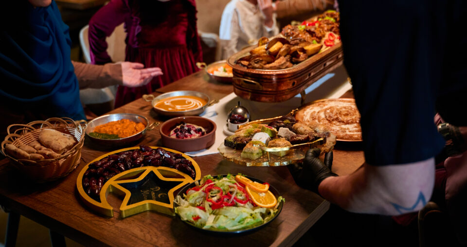 A variety of food on a table with people gathered around it.