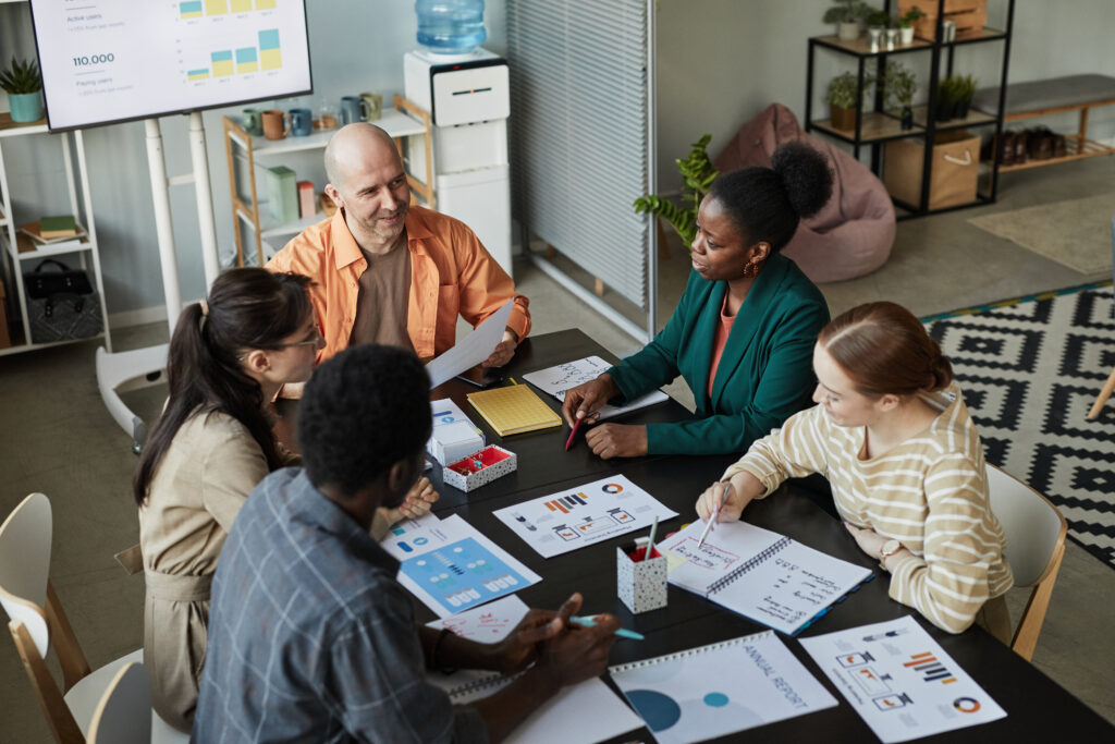 High angle view of creative business team at meeting table discussing project with smiling bald man listening to colleagues