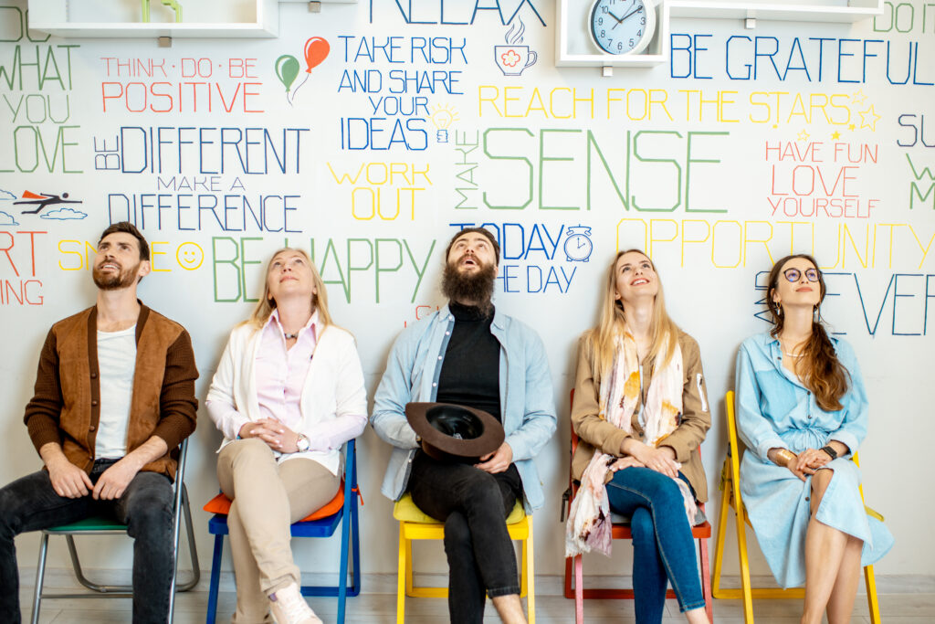 Group of diverse people sitting in a row on the wall background with various inscriptions on the topic of mental health indoors.