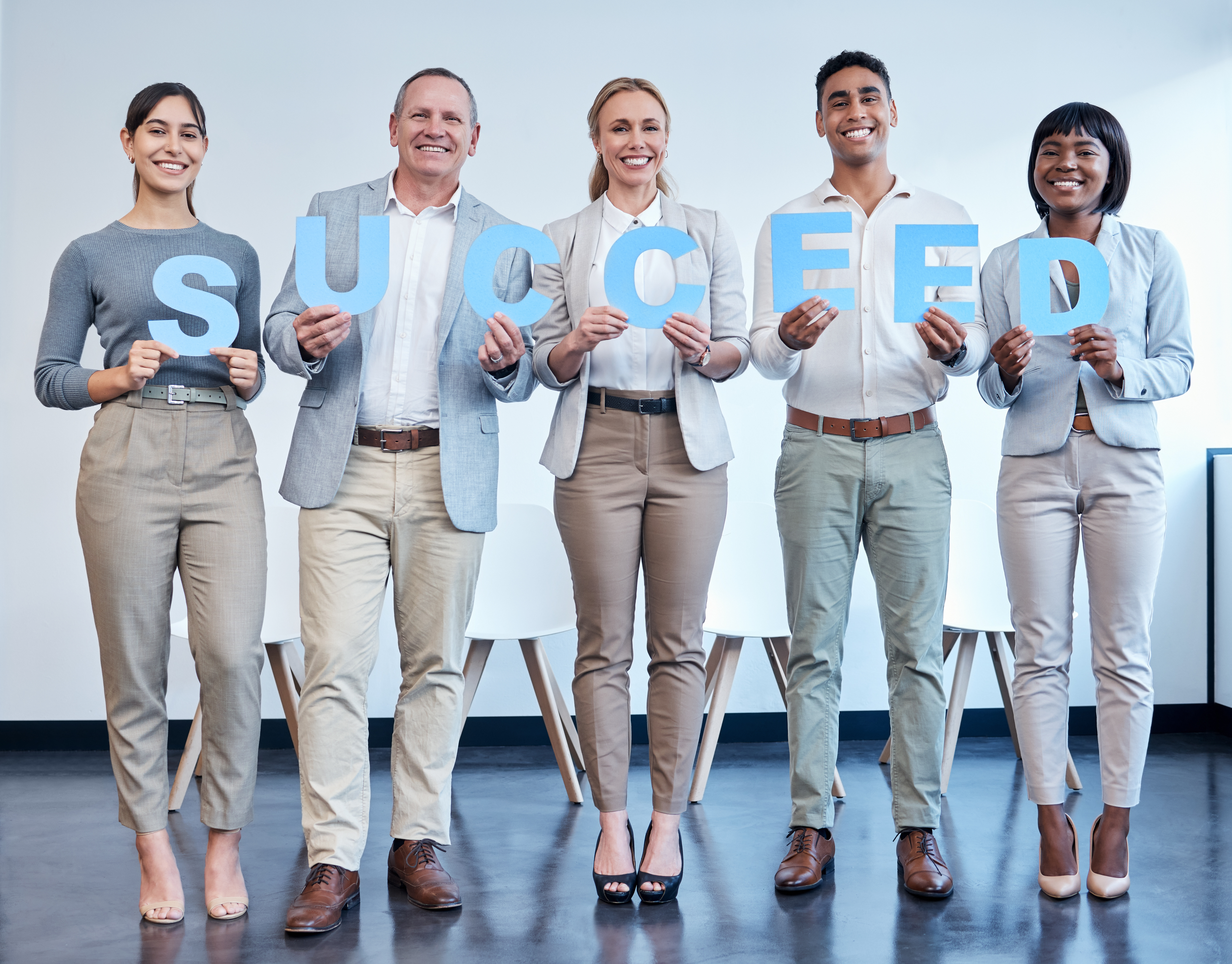 Shot of a group of businesspeople each holding a letter that spells success in an office.