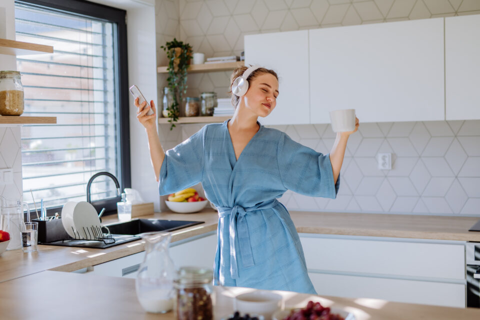 Young woman enjoying cup of coffee and listening music at morning, in a kitchen.