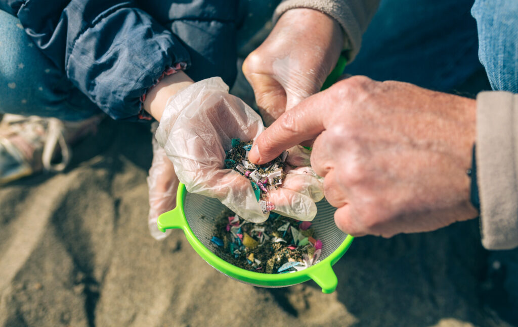 Detail of hands holding colander with microplastics on the beach